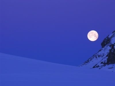 Ein Vollmond erleuchtet eine verschneite Berglandschaft unter einem klaren Nachthimmel.