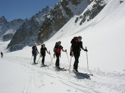 Fünf Skifahrer steigen einen verschneiten Berg hinauf, ausgestattet mit Skistöcken und Rucksäcken, und folgen einer Spur, die von Skispuren gekennzeichnet ist.