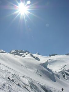 Eine Person, die unter einem hellen Sonnenschein einen schneebedeckten Berg hinunterskit.