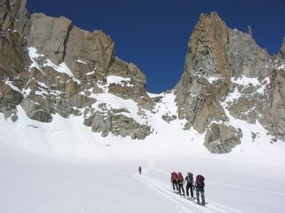 Eine Gruppe von Wanderern mit Rucksäcken durchquert einen verschneiten Bergpfad mit felsigen Klippen im Hintergrund.