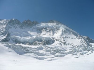 Ein majestätischer schneebedeckter Gebirgszug unter einem klaren blauen Himmel mit steilen Hängen und Felsvorsprüngen.