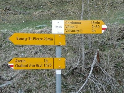 Ein gelbes Wegweiserschild mit mehreren Zielen und Zeitangaben. Es enthält Wegbeschreibungen nach Bourg-St-Pierre, Cordonna, Valsorrey, Azerin und Challand d'en Haut.
