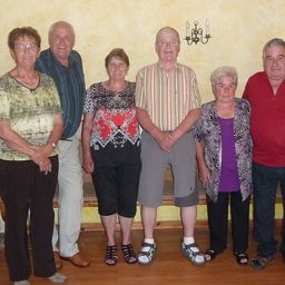 Eine Gruppe älterer Menschen steht für ein Foto zusammen, lächelt und schaut in die Kamera. Sie tragen Freizeitkleidung.