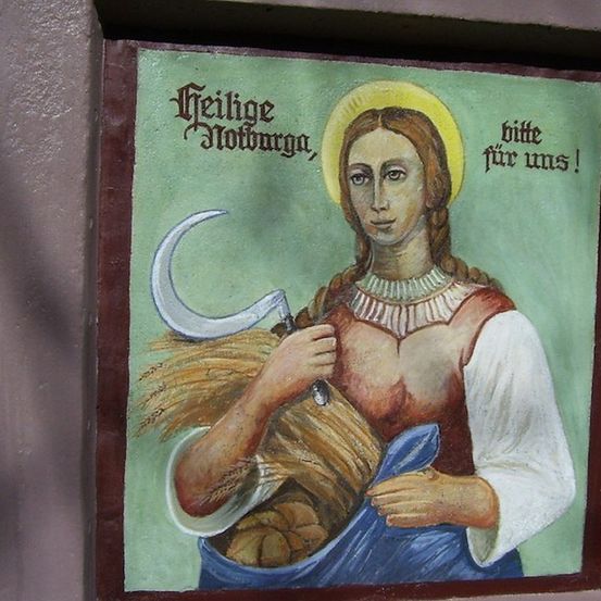 Ein Gemälde einer Frau, die eine Sichel und einen Weizenstoß hält, mit einem Heiligenschein und einem blauen Kleid. Das Gemälde ist mit einem braunen Rahmen versehen.