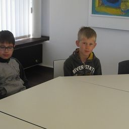 Zwei Jungen sitzen an einem Tisch in einem Raum mit einem Fenster und einem Gemälde an der Wand.