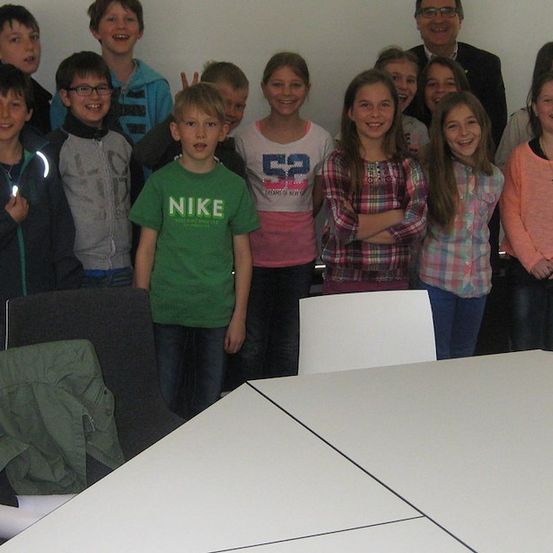 Eine Gruppe von Kindern und Erwachsenen lächelt und posiert für ein Foto im Klassenzimmer.