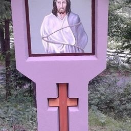 Ein lilafarbener Pfosten mit einem hölzernen Kreuz unten und einem Bild von Jesus Christus in Ketten darauf.