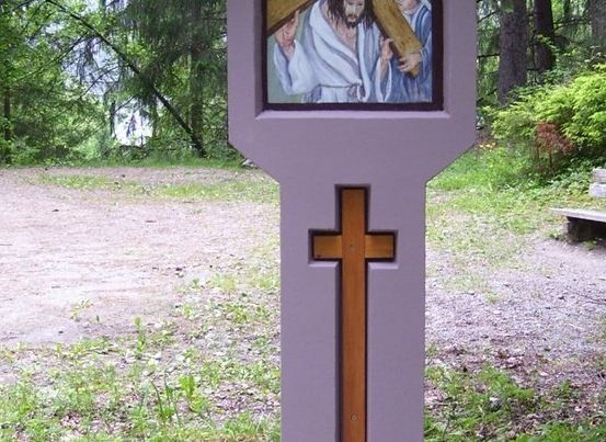 Ein hölzernes Kreuz mit einer religiösen Malerei auf einem Pfosten in einem Park.