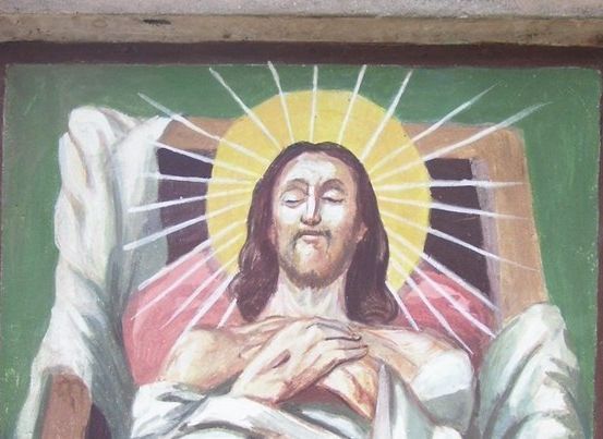 Eine Malerei von Jesus, der auf einem Bett liegt, die Hände über der Brust gefaltet, umgeben von einem hellen gelben Licht.