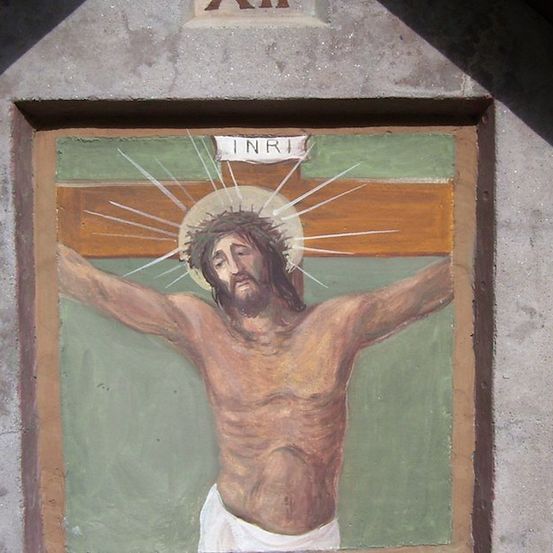 Ein Wandbild, das Jesus am Kreuz zeigt, mit INRI darüber. Das Gemälde ist in einem Betonrahmen eingefasst.