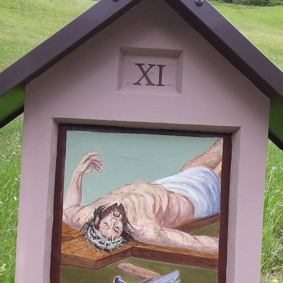Eine kleine, bemalte Box mit der römischen Ziffer XI oben, die eine Szene von Jesus am Kreuz darstellt.