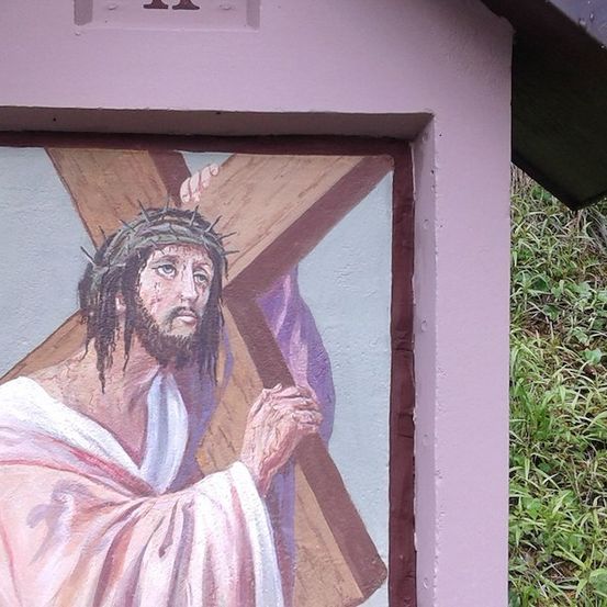 Eine Malerei von Jesus Christus, der ein Kreuz auf einem lila Hintergrund trägt, in einer kleinen, pink gestrichenen Struktur.