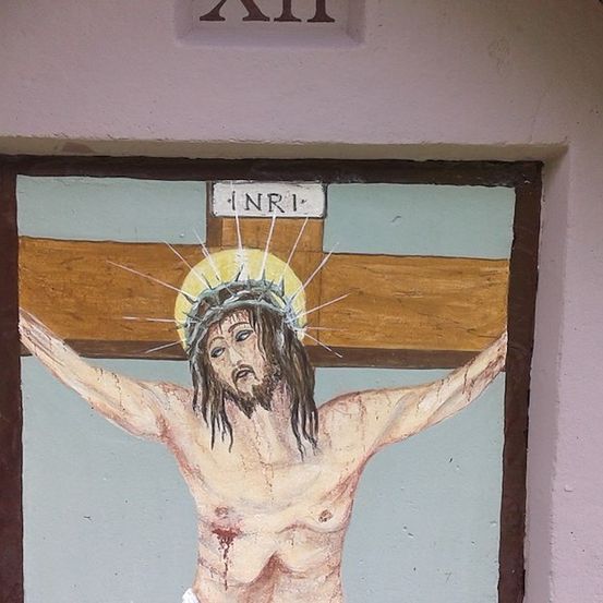 Ein Wandbild, das Jesus am Kreuz zeigt, mit INRI darüber, auf einer Wand gemalt.