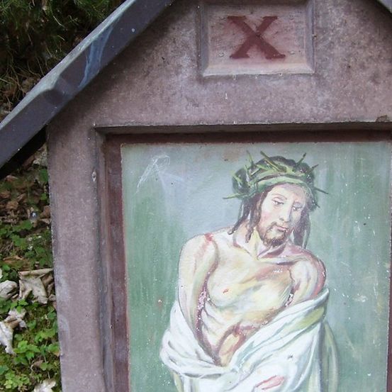 Ein kleines Außenheiligtum mit einem Gemälde von Jesus Christus, der eine Dornenkrone trägt und einen weißen Umhang um die Taille. Oben auf dem Heiligtum befindet sich ein Kreuzsymbol.