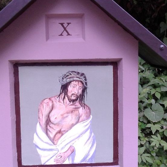 Eine kleine rosafarbene Box mit einem Fenster, das eine Gemälde von Jesus Christus zeigt, der eine Dornenkrone trägt und einen weißen Umhang um die Taille trägt.