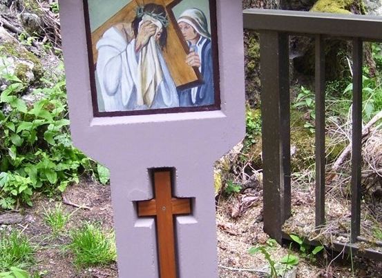 Ein hölzernes Kreuz mit einer Darstellung von Jesus, der das Kreuz trägt, und einer Nonne neben ihm, vor einem natürlichen Hintergrund.