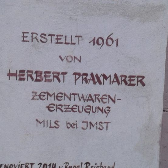 Eine Betonwand mit rotem Text, der 'Erstellt 1961 von Herbert Praxmarer Zementwaren-Erzeugung MILS bei JMST' besagt. Renoviert 2014 von Roger Reichard.