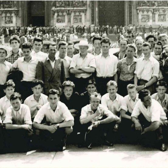 Ein Schwarz-Weiß-Foto einer Gruppe junger Männer, die vor einem historischen Gebäude posieren.