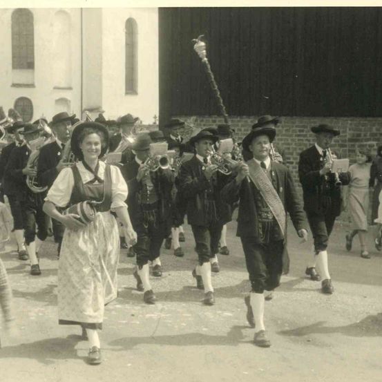 Eine Gruppe von Menschen in traditioneller Kleidung, die mit Musikinstrumenten bei einem Umzug mitmarschieren.
