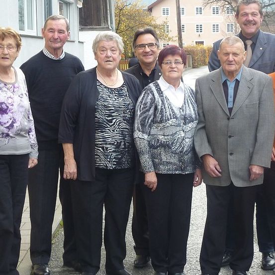 Eine Gruppe älterer Menschen steht zusammen draußen und lächelt für ein Foto. Sie sind in Freizeitkleidung gekleidet und scheinen für ein Familienfoto zu posieren.