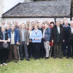 Eine Gruppe älterer Menschen steht vor einem Gebäude. Sie tragen alle Winterkleidung und einige benutzen Gehhilfen.