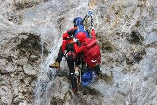 Zwei Personen in roten Jacken werden gerettet, während sie einen felsigen Fels mit fließendem Wasser erklimmen.