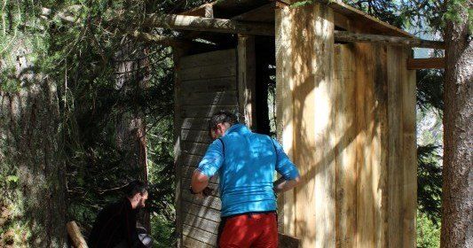 Zwei Männer arbeiten an einer Holzkonstruktion im Wald. Ein Mann ist drinnen, der andere draußen.