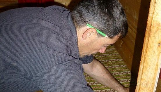 Ein Mann kniet auf dem Boden und schaut nach unten, mit einem grünen Stift im Ohr. Er trägt einen dunklen Pullover.