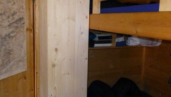 Ein kleiner Raum mit einem holzfarbenen Etagenbett, einer hölzernen Wand und einer Karte links.
