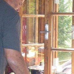 Ein Mann in einem blauen T-Shirt kocht in einer Küche mit einem Fenster, das einen Wald draußen zeigt.