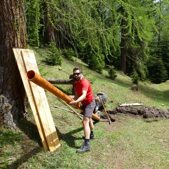 Ein Mann in einem roten Shirt hält eine große Pfeife an einen Baum im Wald.