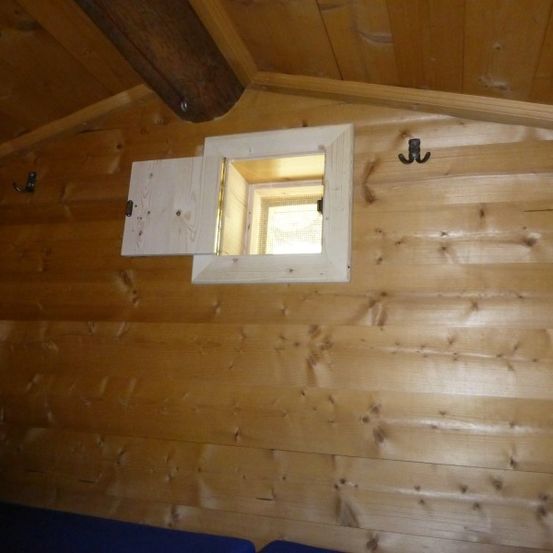 Ein kleines Dachfenster mit hölzerne Rahmen ist geöffnet und lässt Licht in einen Raum mit Holzwänden eintreten.