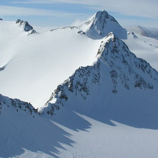 Luftaufnahme von schneebedeckten Bergen mit scharfen Gipfeln und Schatten auf dem Schnee.