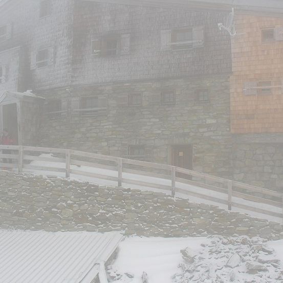 Ein Steingebäude mit einem Holzzaun und einer Gruppe von Menschen in Winterkleidung, die in der Nähe des Eingangs stehen.