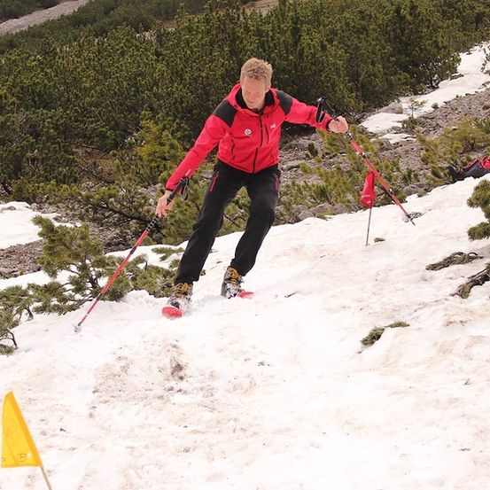 Ein Mann in einem roten Jackett und schwarzen Hosen skifahrer auf einem verschneiten Hügel, mit Skistöcken.
