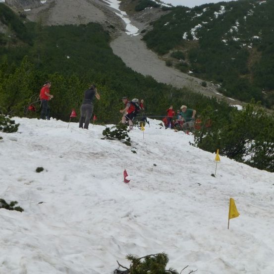 Eine Gruppe von Menschen wandert einen verschneiten Berg hinauf, markiert mit gelben Flaggen.