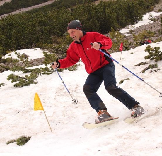 Ein Mann in einem roten Jackett schneidet auf einem verschneiten Berg, hält Skistöcke. Er navigiert um eine gelbe Flagge.