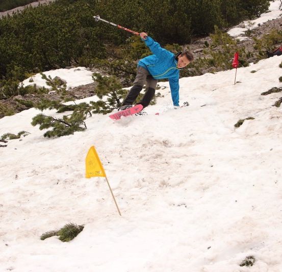 Ein Snowboarder in einem blauen Jacke ist in der Luft und fährt einen schneebedeckten Hang hinunter, mit einer gelben Flagge im Vordergrund.