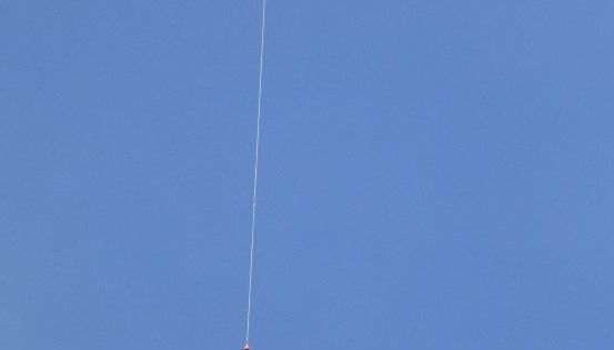 Eine dünne weiße Linie erstreckt sich vom unteren zum oberen Rand des Himmels, mit einem kleinen Objekt, das am Ende hängt.