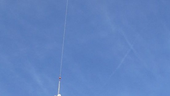 Ein weißes Objekt wird durch ein dünnes Seil am blauen Himmel aufgehängt.