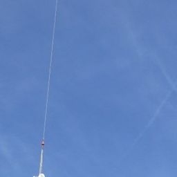 Ein weißes Objekt wird durch ein dünnes Seil am blauen Himmel aufgehängt.