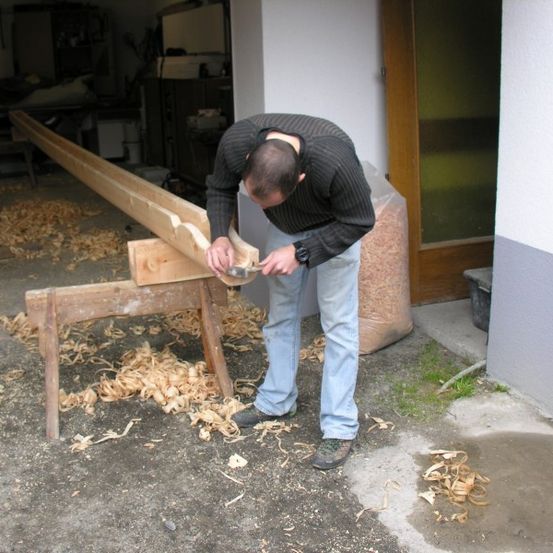 Ein Mann benutzt einen Meißel, um eine Holzplanke auf einer Werkbank in einer Werkstatt zu schnitzen.