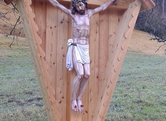 Eine Statue von Jesus Christus, der an einem Holzkreuz genagelt ist, im Freien in einem Grasfeld ausgestellt.