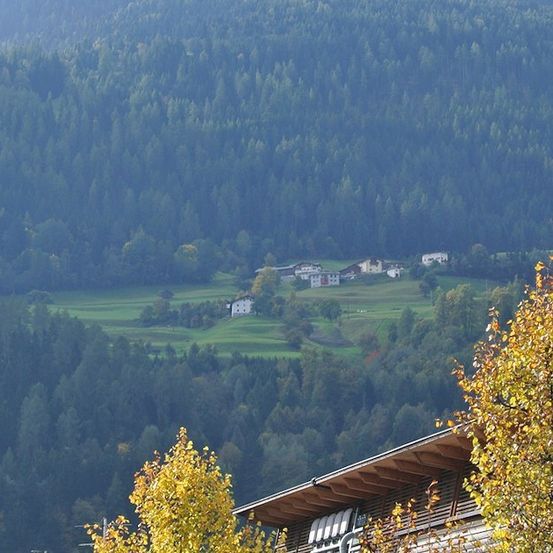 Ein Panoramablick auf eine Berglandschaft mit dichten Wäldern, einem Tal und einigen Häusern in der Ferne.