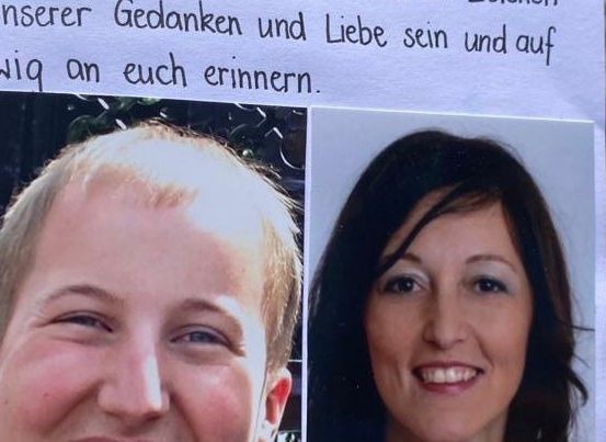 Ein Poster mit zwei lächelnden Gesichtern, einem Mann und einer Frau, und einer handgeschriebenen Nachricht in Deutsch darüber. Der Mann hat kurze blonde Haare und die Frau lange dunkle Haare. Der Hintergrund ist unscharf.