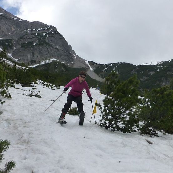Eine Frau in einem rosa Jacke und schwarzen Hosen skis auf einem verschneiten Berg und hält Skistöcke.