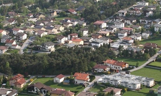 Ein Luftbild einer kleinen Stadt mit vielen Häusern, grünen Rasenflächen und Bäumen. Die Stadt ist von einer üppigen grünen Landschaft umgeben.