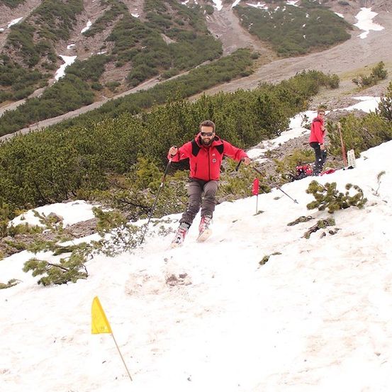 Ein Mann in einem roten Jackett skifahrer auf einem schneebedeckten Hang mit einer gelben Flagge im Vordergrund.