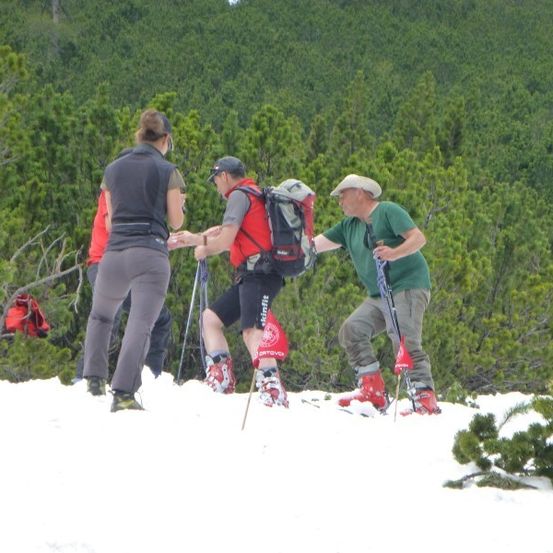 Eine Gruppe von Menschen wandert im Schnee mit Skiern und Stöcken. Sie tragen Winterkleidung und Rucksäcke.