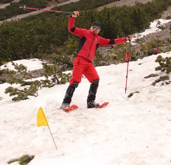 Ein Mann in einem roten Schneeanzug skifahrer auf einem verschneiten Berg und hält Skistöcke.